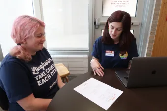 A Longhorn TIES student with pink hair sits at a table and looks at a worksheet with a Longhorn TIES coach.