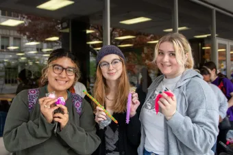 Three friends smile at the camera while holding fidgets from Fidget Friday.