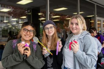 Three friends smile at the camera while holding fidgets from Fidget Friday.
