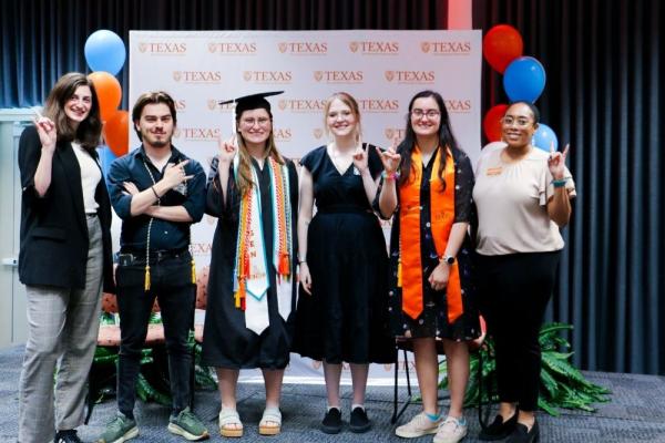 Longhorn TIES graduates and Longhorn TIES staff smile and hold Hook 'Em Hands in front of a sign at Disability Graduation 2025.