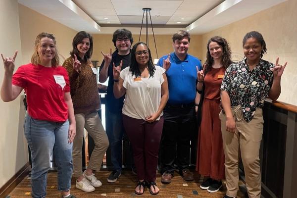 A group of smiling TIESplus graduates stand with Longhorn TIES staff members making the Hook 'Em hand symbol.